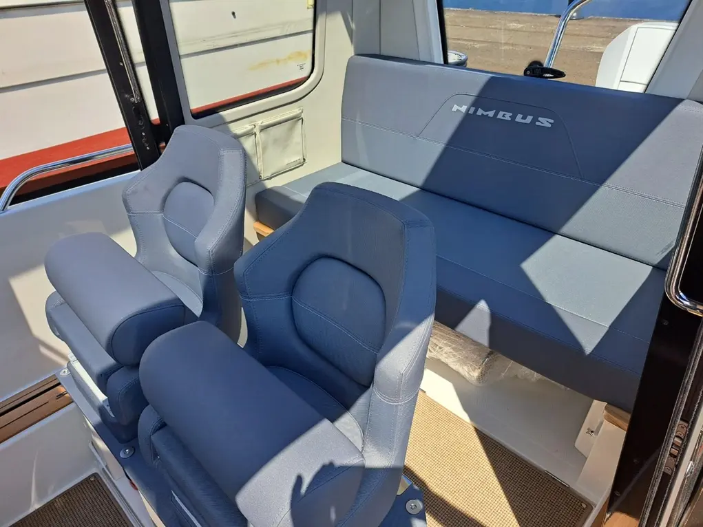 Interior of a Nimbus boat featuring two blue captain's chairs and a cushioned rear bench, highlighted by sunlight.